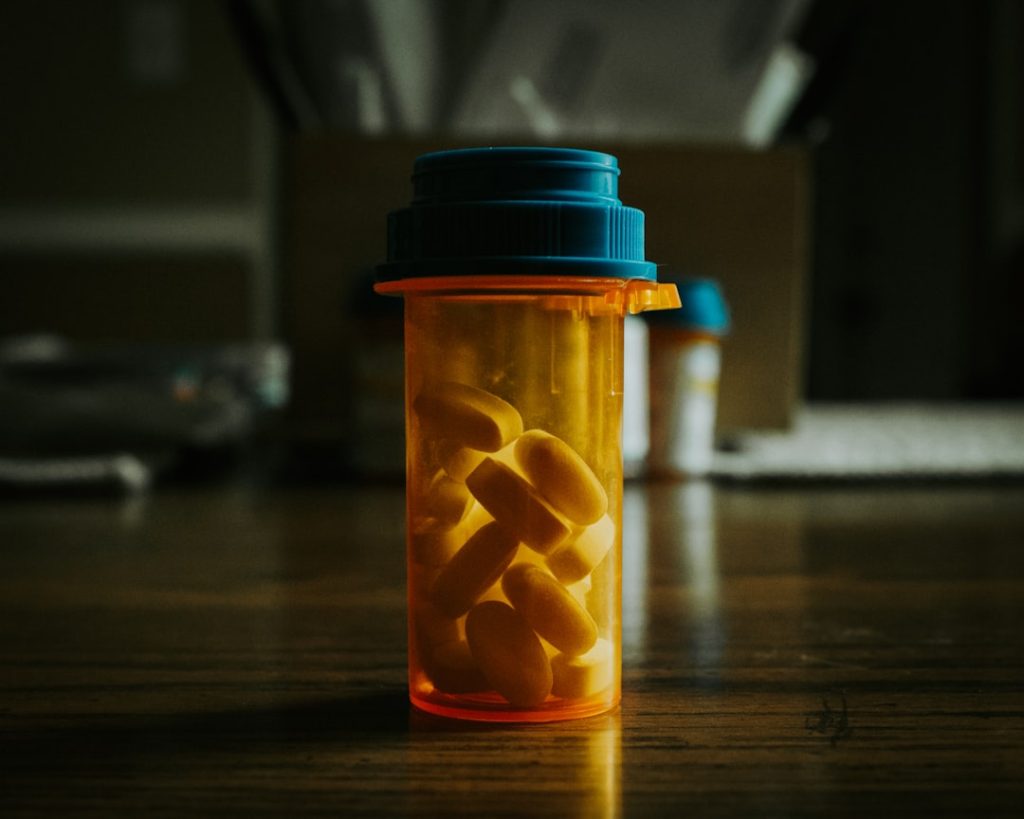 Close-up of an orange prescription bottle filled with yellow pills on a wooden surface