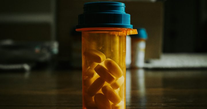 Close-up of an orange prescription bottle filled with yellow pills on a wooden surface